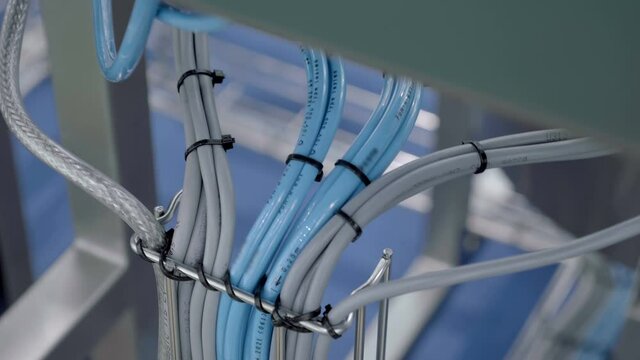In industrial production many wires of gray and blue colors are laid in a metal tray and diverge to their equipment. Shot in motion. Closeup