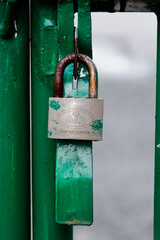 Silver metal and rustic padlock hanging on the locked green iron fence with blurry and soft focus...
