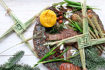 Wiccan altar for Imbolc sabbat. winter-spring pagan festive ritual. Brigid's cross, wheel of the year, snowdrops, sun and moon symbol on wooden table. Imbolc holiday, spring equinox. top view - obrazy, fototapety, plakaty
