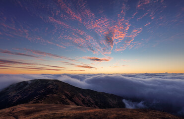 Fabulous sunset high in the mountains above the clouds. Aerial view of dramatic mountain landscape at dusk with fog and soft light.