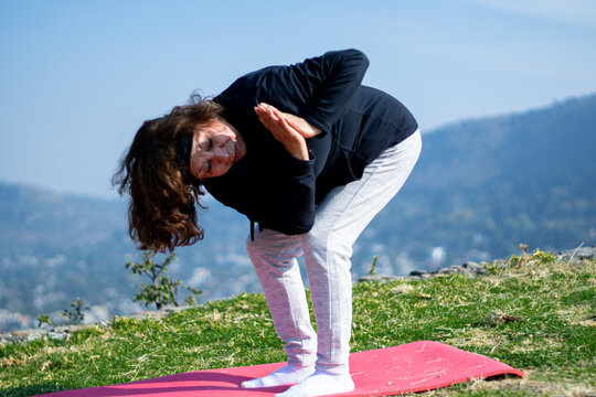 Senior Woman Doing Revolved Chair Pose, Group Yoga Practice Outdoors, Exercise On Mountain Esplanade. Healthy, Health, Selective Focus, Blur