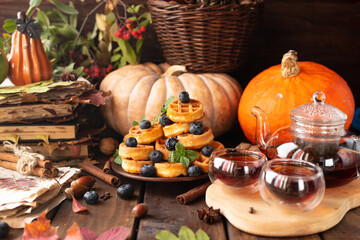 many waffles are stacked on a plate, decorated with mint leaves and blueberries. Tea in a glass teapot and two small bowls