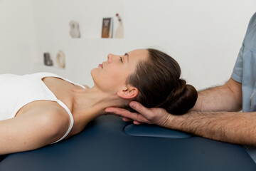 Female patient receiving osteopathic neck and shoulder treatment. Therapist manipulating back of...
