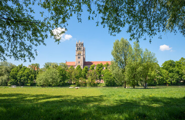 Fototapeta na wymiar recreational area Isar river munich, green meadow, view through willow branches to church St. Maximilian