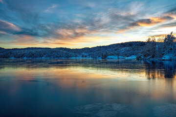 Ice covered fjord and colorful sky reflected in the ice. Winter landscape with islands, huts, sea, snowy rocks, blue sky, reflection at sunset. , Norway at dusk. Nature