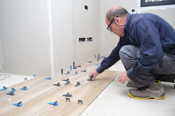 Senior mason laying ceramic wood effect tiles using tile levelers.