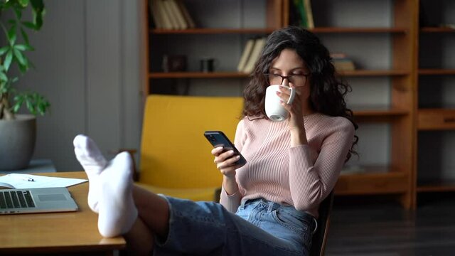 Joyful girl young businesswoman or remote employee relax from work using cellular application for social networking at coffee break in home office. Millennial woman read sms messaging on mobile phone