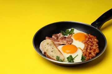 Pan with tasty breakfast on yellow background
