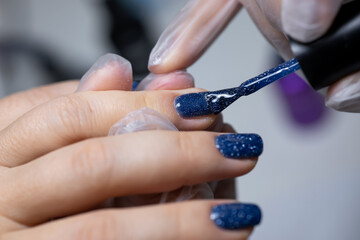 the manicure master performs the final stage of applying gel polish to the nail surface with a brush
