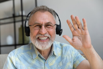 Head shot happy old mature man wearing headphones with mic waving hand looking at camera, starting...