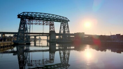 Sunrise view of the historic monument of Puente Transbordador Nicolas Avellaneda bridge with beautiful refection on Riachuelo river, low level aerial stationary shot.