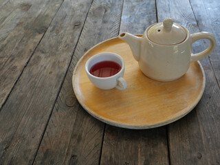 Red Color Tea Rose Petals in white cup and ceramic teapot on wooden tray on brown table