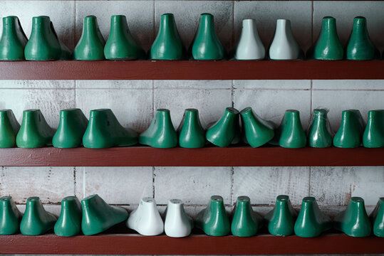 Rows of shoe lasts for shoemaking. Pairs of plastic green and white lasts on shelves. Shoemaker tools in workshop.