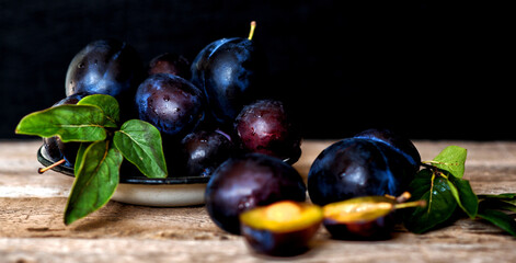 Ripe plum with green leaves on rustic background. Ripe fresh organic plums.