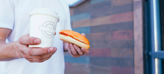 Man hand holding in hands hot cappuccino in white takeaway paper cup. Coffee take away at cafe shop. Closeup in man hands. Street food, fast food.