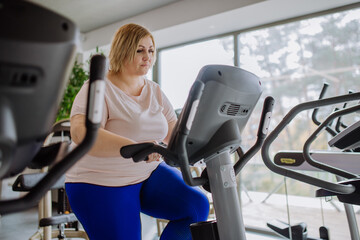 Happy mid adult overweight woman exercising on stepper indoors in gym