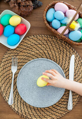 Little girl's hand putting yellow Easter egg on a plate