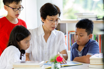 A Group of Asian Student Kid Reading a book with women teacher in School library with Shelf of Books in Background, Asian Kid Education Concept