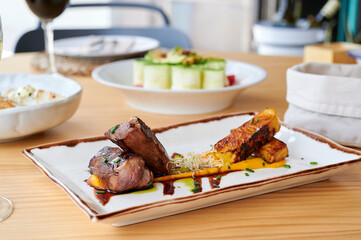 Eater view of plate with delicious BBQ pork and pineapple served with sauces on wooden table with more blurred food on background