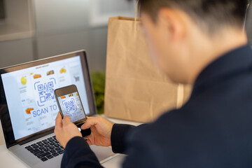 Fototapeta na wymiar Man using smartphone for payment in online store on laptop on kitchen at home. Concept of online shopping and e-commerce. Idea of healthy and vegetarian eating. Person sit at table with shopping bags