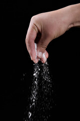 Male hand sprinkles salt on a black background. Cooking concept.