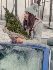Young girl seats in the car cabrio with little christmas tree