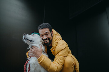 Happy young man hugging his dog outdoors in winter against dark background.