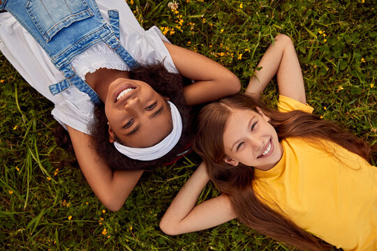 Positive diverse little friends lying on blooming meadow and smiling