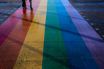 feet of couple walking on asphalt with colors of the LGBT flag