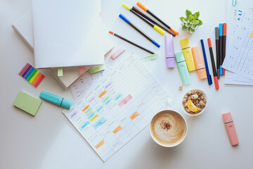 Top view of the white work desk with colourful stationery. Student's schedule for the week. Planning a working week with coffee and snacks. layout.