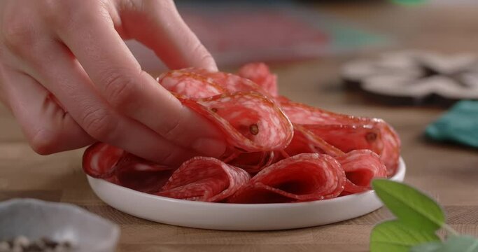 Woman puts sliced salami to the plate by fingers in slow motion. Cooking with pepperoni, 4k 60p Prores