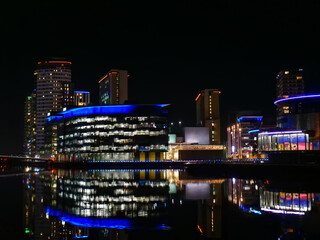 Vibrant reflections of modern buildings in Salford, Greater Manchester on calm dark water at night, copy space.