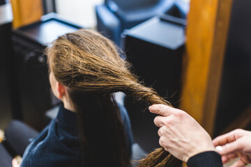 Naklejka premium Master woman hairdresser carefully applies a special conditioner for hair after washing the girl's head in a beauty salon