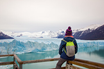 Young woman, girl with backpack looks at Perito Moreno glacier in Patagonia. Floe located in Los Glaciares National Park, in the southwest of the Argentine province of Santa Cruz, El Calafate - obrazy, fototapety, plakaty