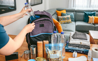 Unrecognizable woman putting a water bottle to prepare emergency backpack in living room - Powered by Adobe