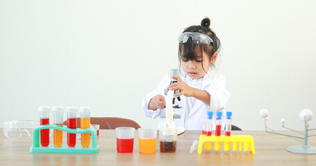 Little girl asian cute little student child learning research and doing a chemical experiment while making analyzing and mixing liquid in test tube at home on the table.