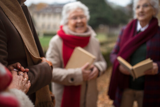 Group of happy senior friends with books on walk outdoors in park in autumn, reading and talking.