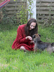 Young female sitting on green grass with small dog. Woman playing with cute dog in the garden. Summertime fun. 