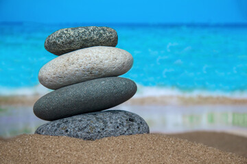 Fototapeta na wymiar Buddhist cairn, sea pebbles pyramid in the sand on the background of beach and sea. Concept of relaxation