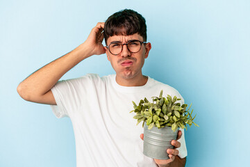 Young mixed race man holding a plant isolated on blue background being shocked, she has remembered...