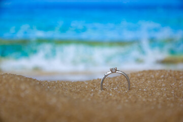 One engagement silver ring in the sand on the background of beach and sea.