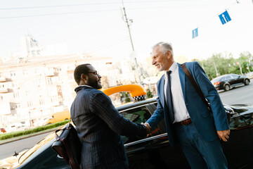 Multiracial men smiling and handshaking while standing by taxi