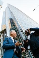 Multiracial men talking and gesturing while standing by building