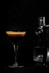 Espresso martini cocktail with vodka, coffee liqueur, syrup and ice, dark bar counter background, bar tools, copy space