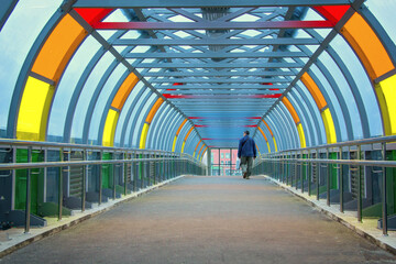 Man crosses the road over the bridge. Glass overhead passage through the highway. Bright multi-colored glass on a metal frame. New Moscow