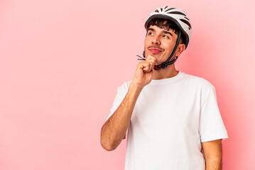Young mixed race man wearing a helmet bike isolated on pink background looking sideways with doubtful and skeptical expression.