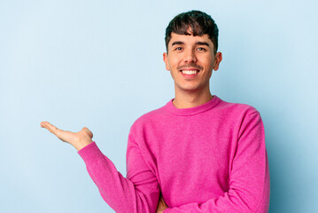 Young mixed race man isolated on blue background showing a copy space on a palm and holding another...