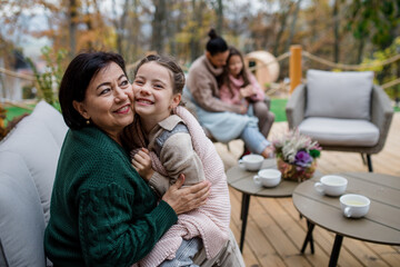 Happy little girl with grandmother sitting wrapped in blanket outdoors in patio in autumn