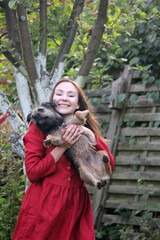 Smiling young woman holds funny border terrier dog. Female in red dress with cute dog. Summer outdoor photo. Playing with puppy in the garden. 