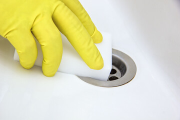 Cleaning the bathroom with melamine sponge. A gloved hand holds a sponge, wipes the plumbing from...
